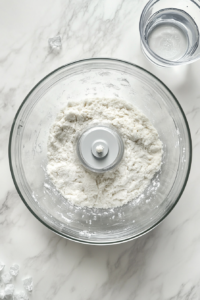 This image shows water being added to the processed ingredients in a food processor to form a cohesive dough for the pie crust.