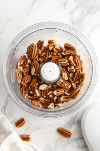 this image shows raw pecans being ground in a food processor to create a fine, crumbly texture, forming the base of the crust for the chocolate truffle pie.