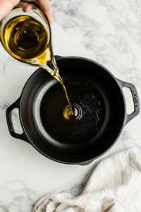 This image shows olive oil being heated in a Dutch oven, preparing the base for a rich and creamy vegan corn chowder.
