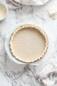 This image shows the tart crust lined with a sheet of baking parchment, weighted down with pie weights or beans to prevent puffing.