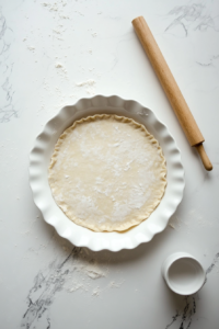 This image shows a pie pan lined with a rolled-out crust, edges trimmed and ready to be filled with the cherry mixture.