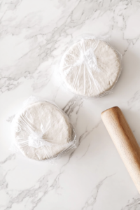 This image shows a rolling pin smoothing out the dough into a thin, even layer on a floured countertop, preparing it for the pie crust.