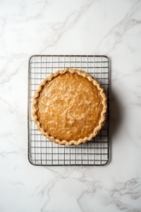 This image shows the freshly baked sweet potato pie resting on a wire rack, cooling before being sliced and served.