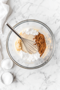 This image shows a bowl filled with pumpkin purée, brown sugar, and spices being whisked together to create a smooth and aromatic filling for the vegan pumpkin pie.