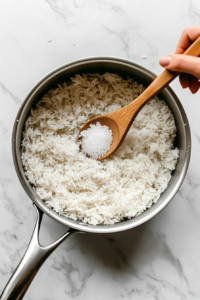 This image shows water and salt being poured into a saucepan with toasted rice, an essential step for achieving fluffy and flavorful rice.