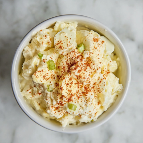 This image shows a creamy egg salad made with chopped hard-boiled eggs mixed in mayonnaise and mustard, topped with vibrant paprika and arranged neatly on a plate.