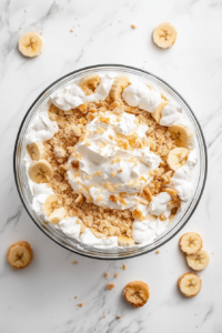 multiple-delicious-layers-of-banana-pudding-whipped-cream-and-pound-cake-being-stacked-in-glass-bowl
