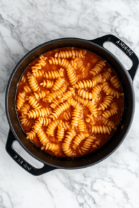 black-dutch-oven-simmering-shell-pasta-in-creamy-tomato-broth-on-white-marble